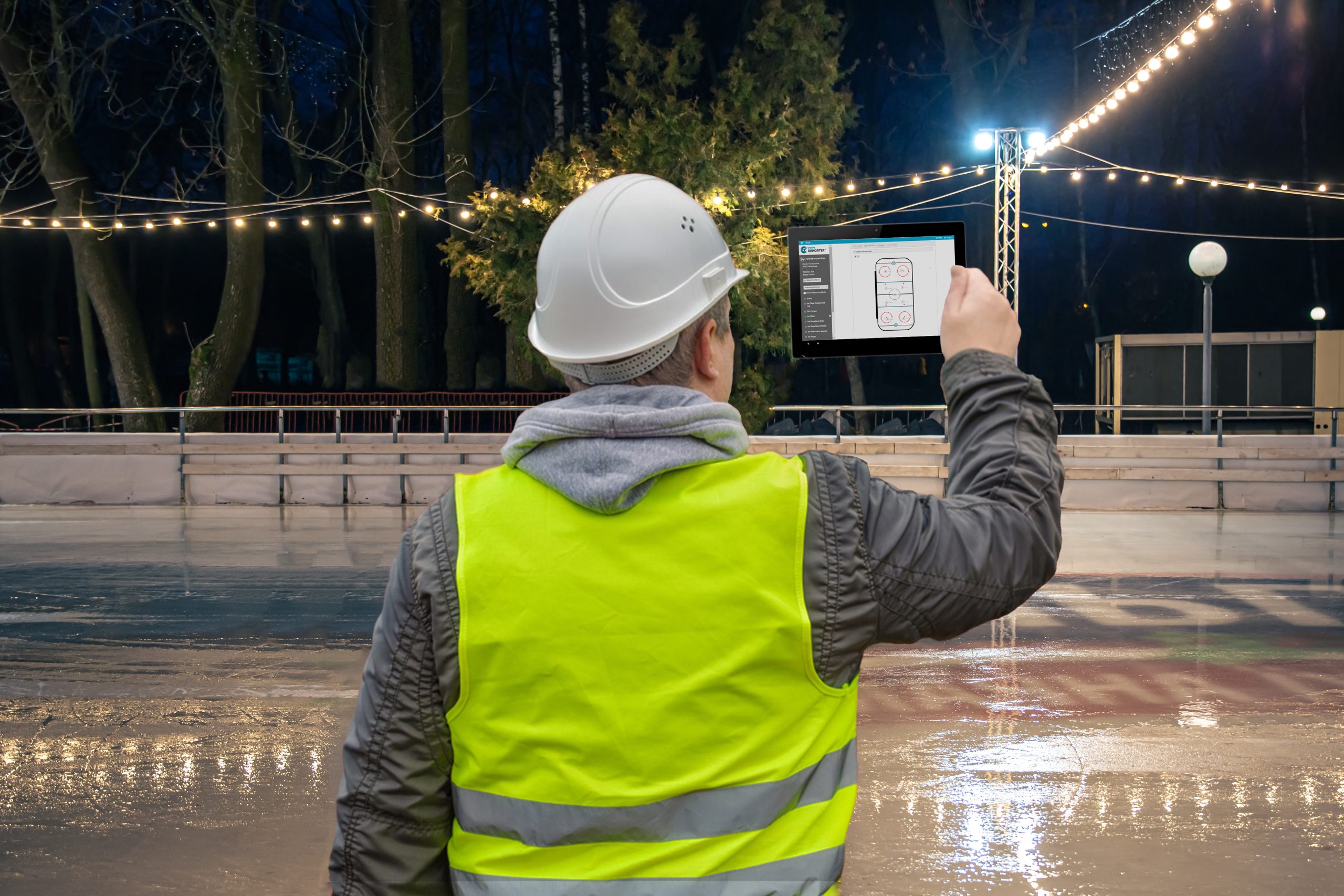 A public works employee conducting a ice tap inspection on an ice rink using inspection software to map the data